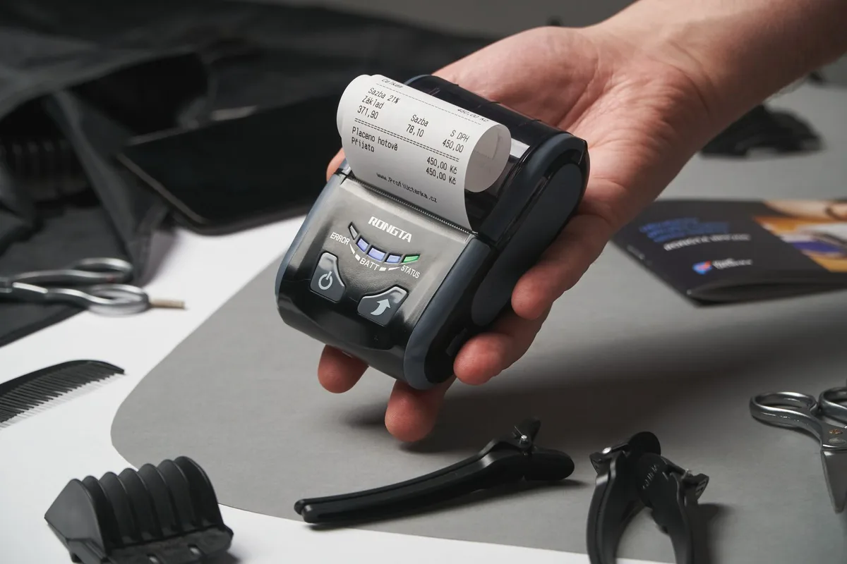 A portable thermal printer held in a hand, actively printing a receipt