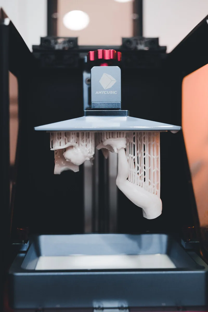 Resin 3D printer with the build plate lifted out of the vat, showing cured parts with support structures